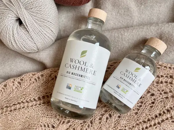 Zwei Flaschen "Wool & Cashmere" Bio-Waschmittel neben Garnknäueln und Strickwaren. Perfekt für die sanfte **Wolle waschen mit Shampoo**.