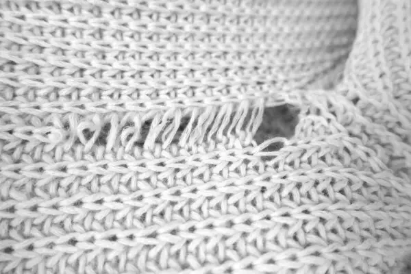 Nahaufnahme eines verfilzten und eingelaufenen Pullovers. Die Strickstruktur ist sichtbar, mit ausgefransten Fäden und einem Loch.