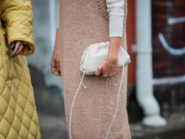 Ein gelber Steppmantel und ein Strickkleid mit weißem Langarmshirt darunter – ein perfekter layering look. Eine weiße Clutch rundet das Outfit ab.